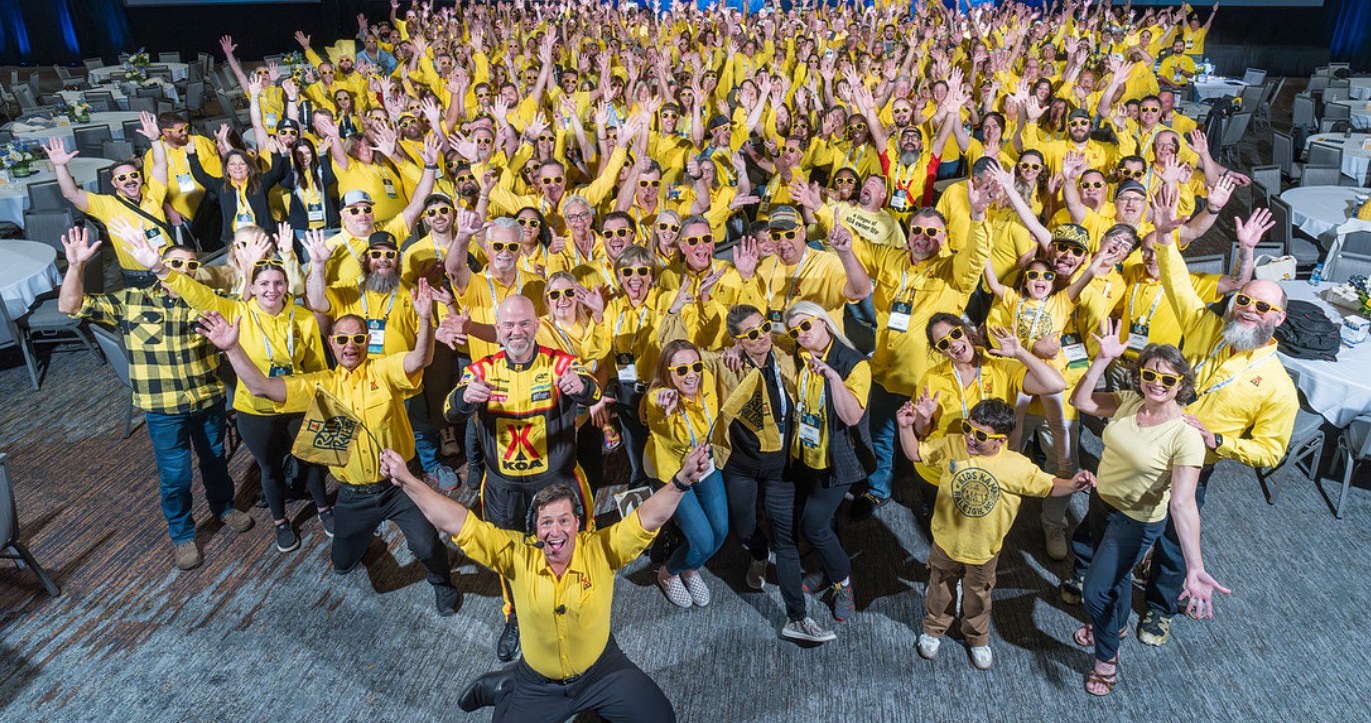 Hundreds of KOA owners in yellow shirts with their hands raised for the annual convention group photo